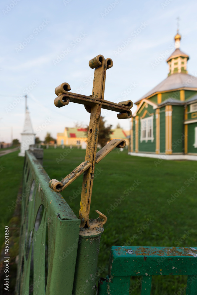 Old iron rusty Orthodox cross on an old fence. Orthodox church in the background.