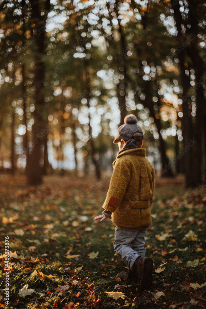 Stylish boy having fun in autumn city park. Happy kid walking among fallen leaves. Kids fashion. Boy wearing trendy yellow coat, cap and scarf. Smiling young boy outdoors. Kid jumping and run Stylish boy having fun in autumn city park. Happy kid walking among fallen leaves. Kids fashion. Boy wearing trendy yellow coat, cap and scarf. Smiling young boy outdoors. Kid jumping and run