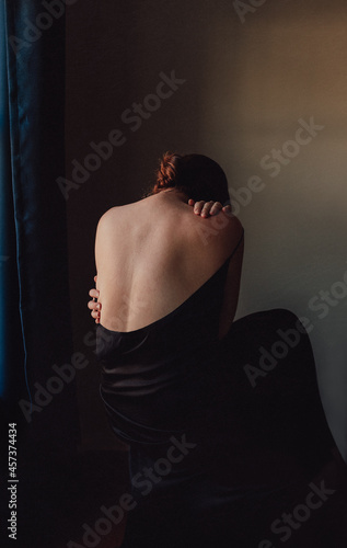 Back view of sad woman bent forward with back exposed in a dark room.