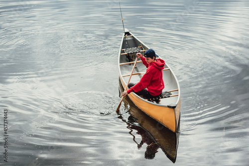 Teen boy paddling a canoe alone on a calm lake in Canada.