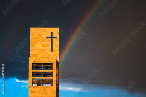 A rainbow above a modern church tower with christian cross, image with copy-space