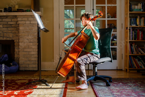 A barefoot boy practices cello in golden window light indoors photo