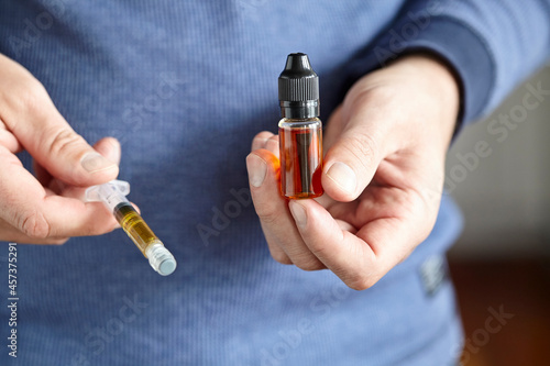 hands holding a syringe of co2 oil and a bottle of cannabis distillate photo