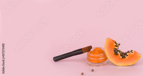 Slice of orange papaya with cream in a jar and a brush on a pink background. Natural cosmetics concept.