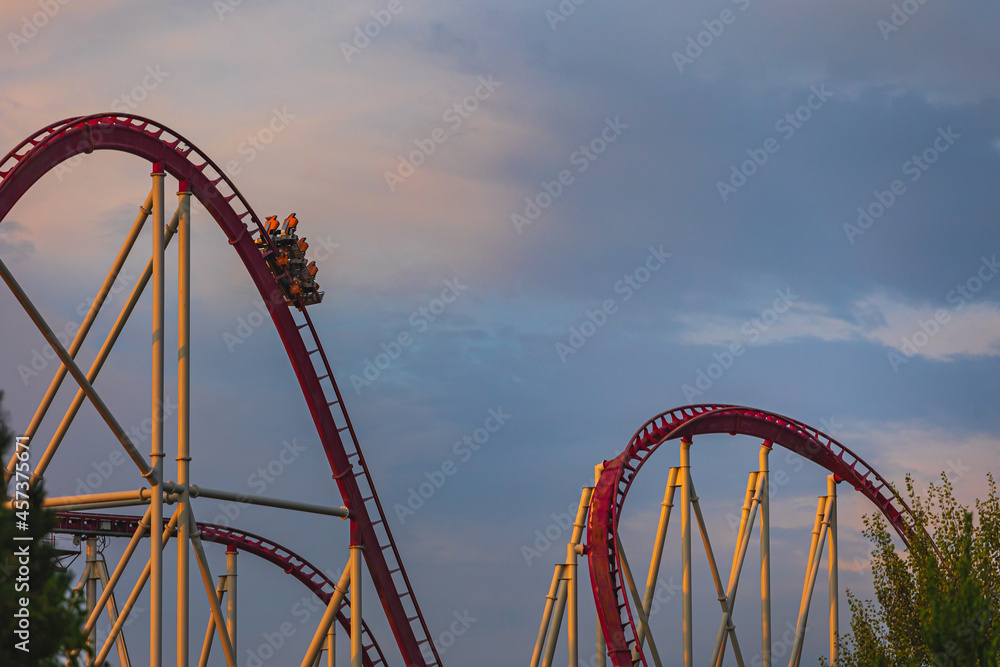 The train with some people is riding on roller coaster during the sunset