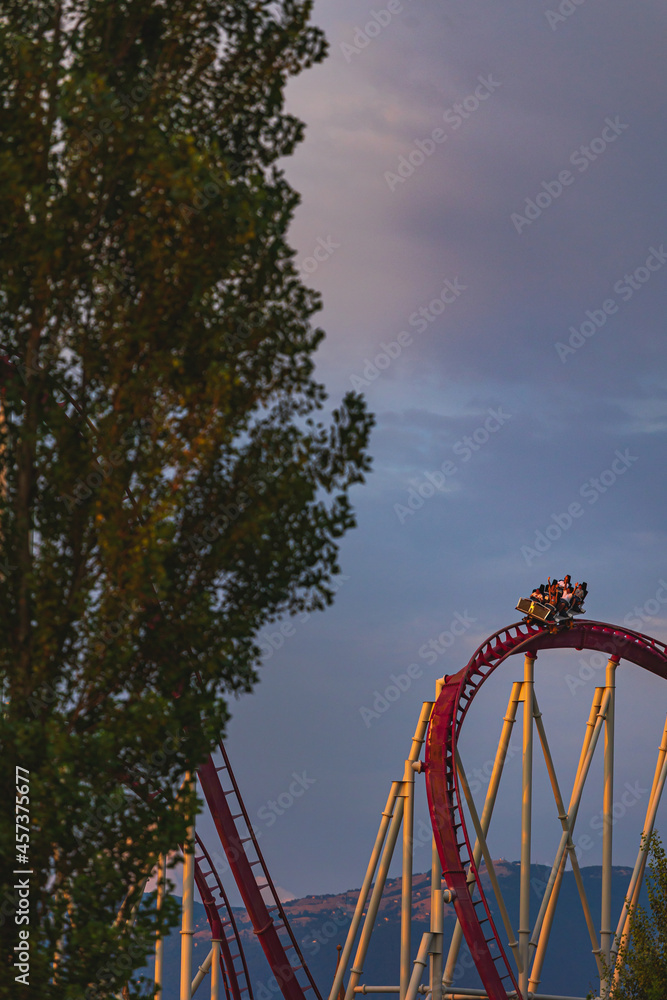 The train with some people is riding on roller coaster during the sunset The train with some people is riding on roller coaster during the sunset
