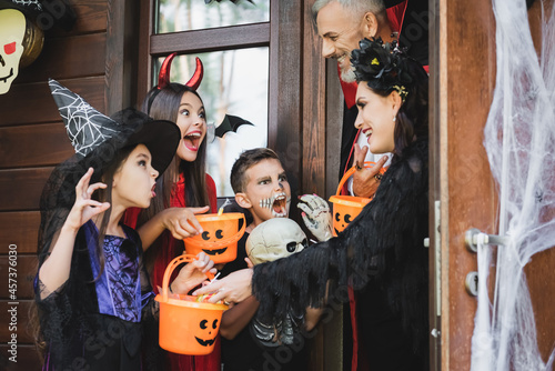 children in creepy halloween costumes holding buckets and growling at smiling parents
