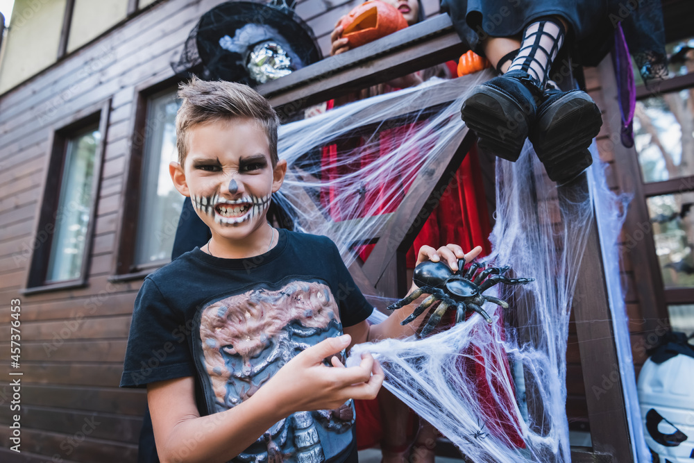 grimacing boy in skeleton costume playing with toy spider near sisters
