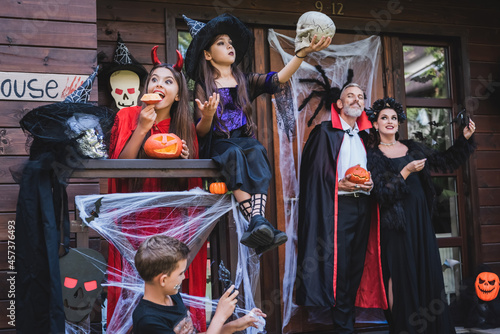 family in spooky costumes having fun on cottage porch with halloween decoration