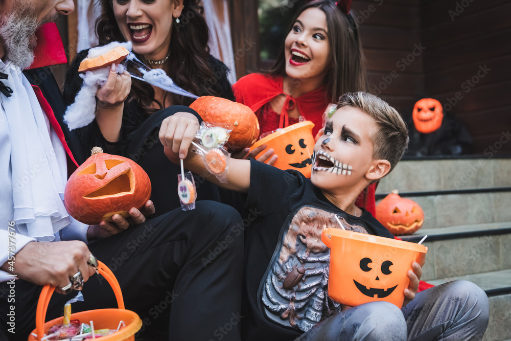 excited boy holding lollipops near family in halloween costumes