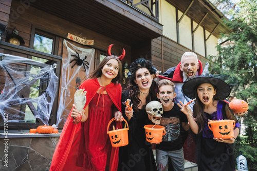 cheerful family in spooky halloween costumes grimacing at camera near house