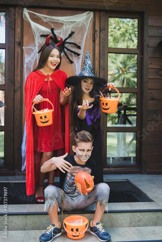 boy pointing at carved pumpkin near spooky sisters holding buckets with sweets and showing come here gesture