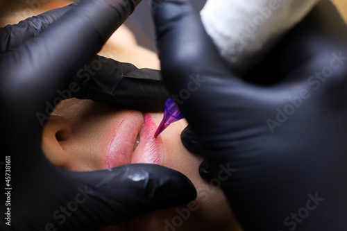 close-up of the master working with a lip tattoo on the lower lip of the model