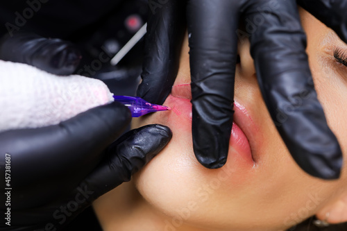 in the cosmetology office, a tattoo artist performs the procedure of permanent lip makeup
