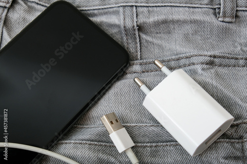 Usb charger, wire and adapter plug and a smartphone in grey jeans pocket, dont forget charger at home photo