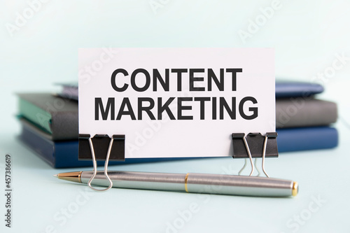Foto a white card with content marketing text stands on paper clips on a desk against