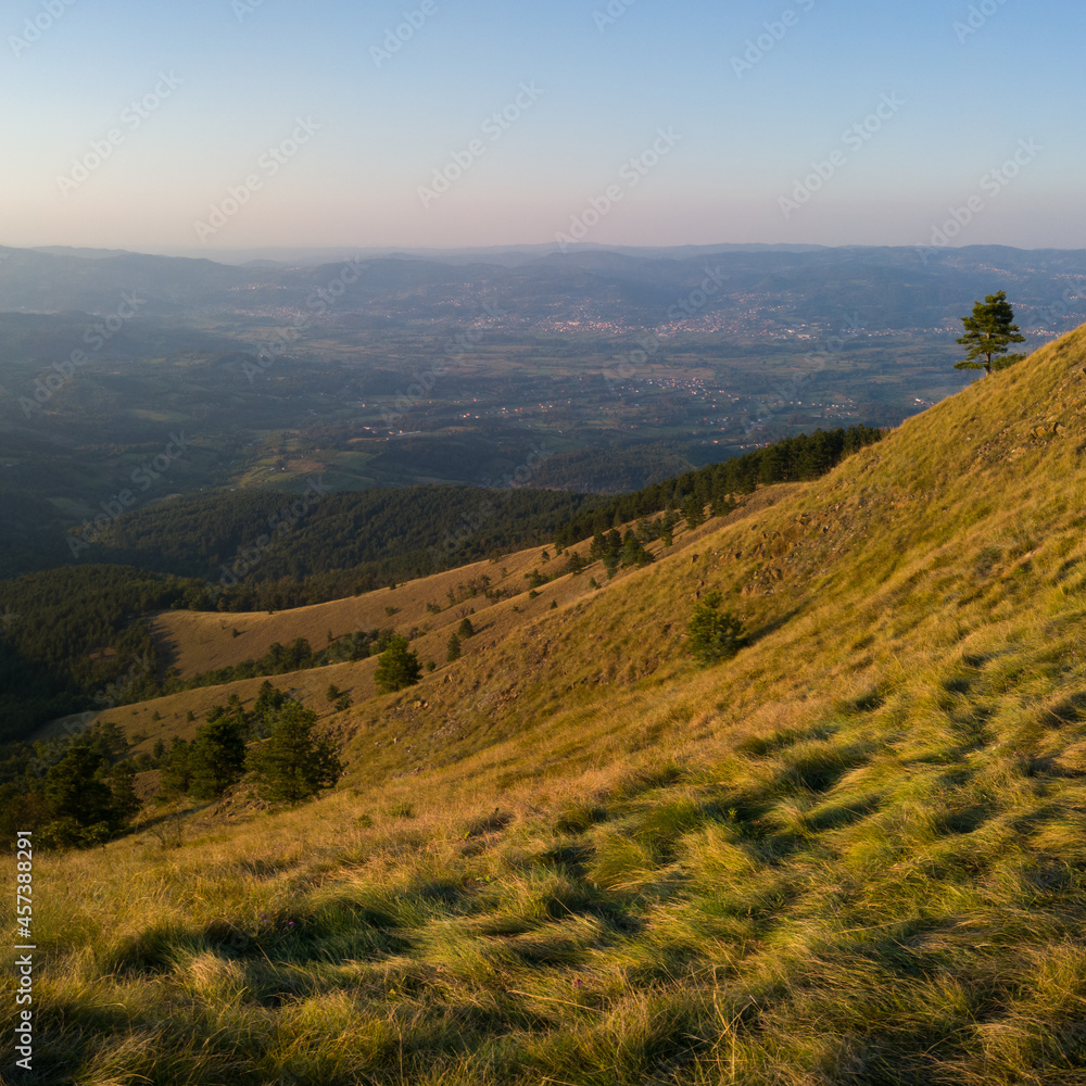 View from the top of Gostilj on the mountain Ozren on the slopes and villages in the valley, a landscape of hilly Balkans with haze on the horizon at evening