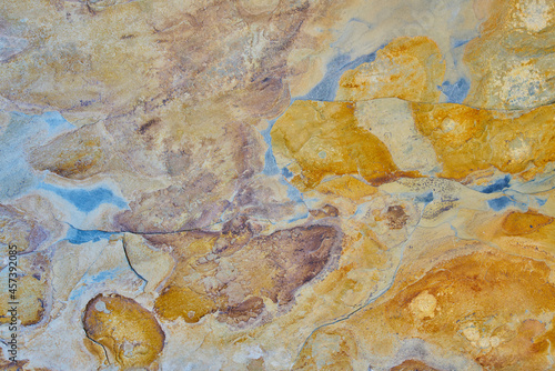 Rough stone texture with rust in blue and yellow colors with orange placed on a wall on a facade