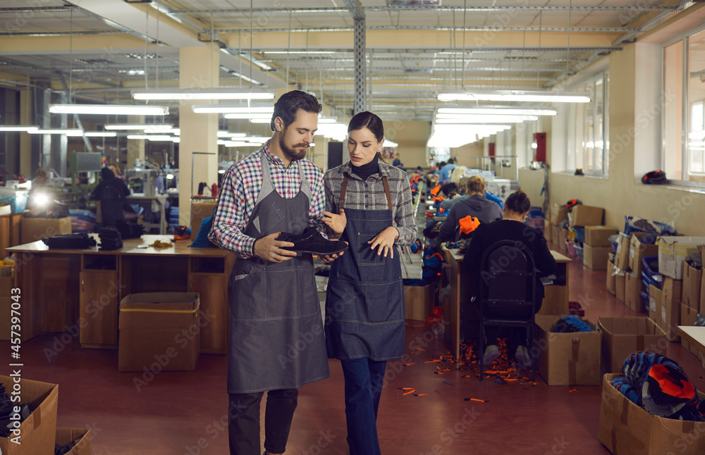 Two Caucasian shoe factory workers looking at leather boot and discussing quality of new