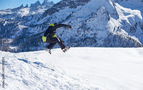 Chłopiec w stroju narciarskim wykonujący skok ze śnieżnej góry. Zimowy krajobraz górski, w tle skaliste, ośnieżone szczyty górskie.