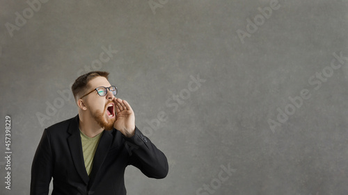 Don't miss it. Active man who shouts, announcing advertising information standing on a gray background. Emotional man announces crazy discounts. Advertising banner. Place for text.
