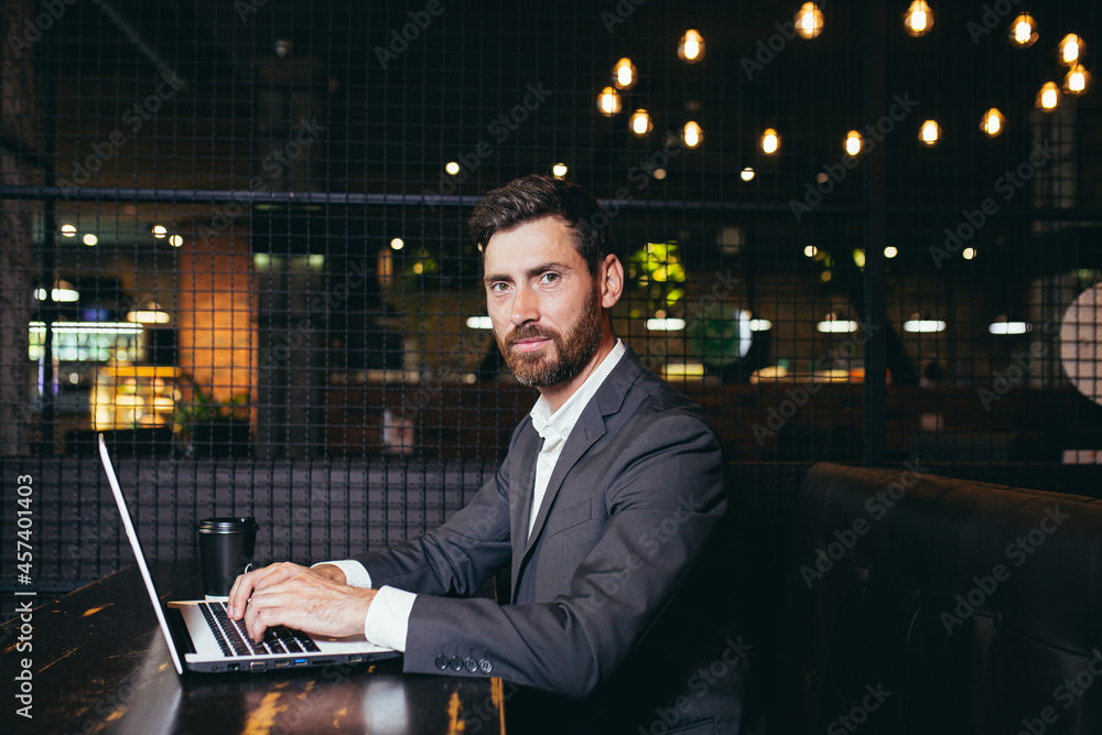 Successful businessman working on laptop during lunch break sitting in hotel restaurant serious looking at camera with cup of coffee Successful businessman working on laptop during lunch break sitting in hotel restaurant serious looking at camera with cup of coffee
