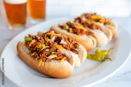Photography Close up of a plate of chili dogs with glasses of beer in background