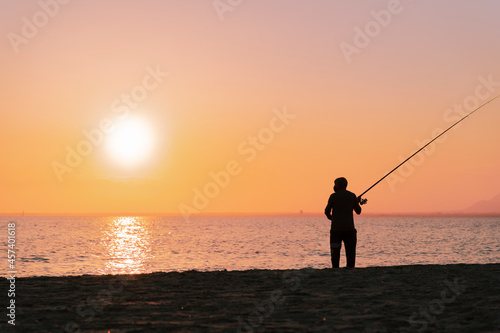 Silhouette of man fishing in waves on beach at sunset