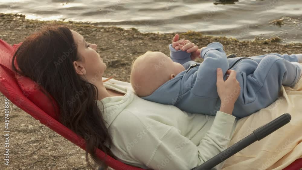 Mother and baby boy against water surface with sun glint, love, friendship and active happy family on summer vacation. High quality 4k footage Mother and baby boy against water surface with sun glint, love, friendship and active happy family on summer vacation. High quality 4k footage