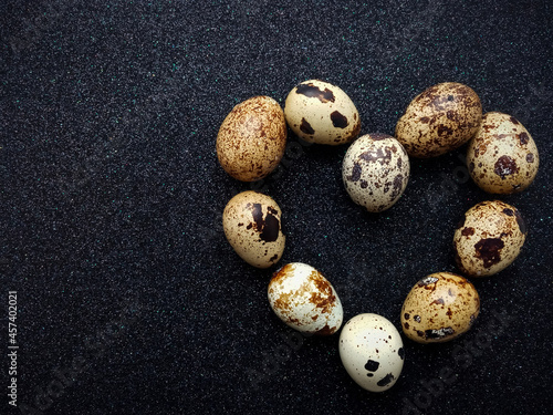 Fototapeta tten quail eggs in the shape of a heart on a black background closeup