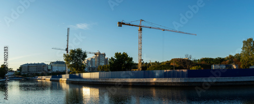 Construction site in the city centre with a couple of tall yellow cranes for lifting heavy construction material and tree on blue sky background. Construction industry. Space for text.