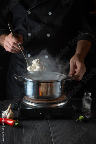Professional chef cooks meat dumplings in a saucepan in the restaurant kitchen. Close-up of the hands of the cook during work