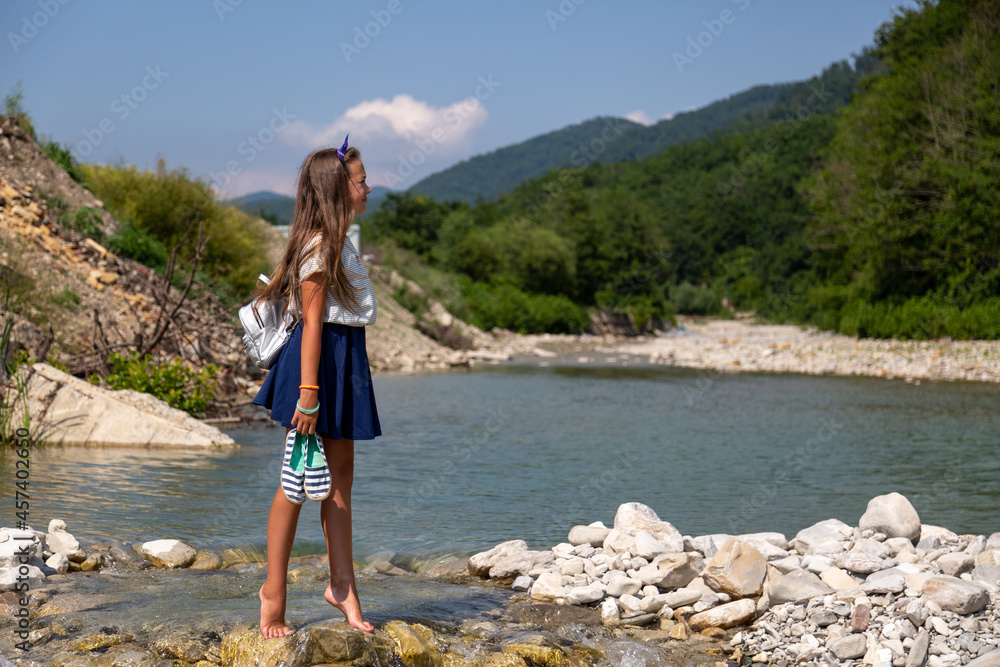 a girl walks barefoot on stones among the mountains on a sunny day