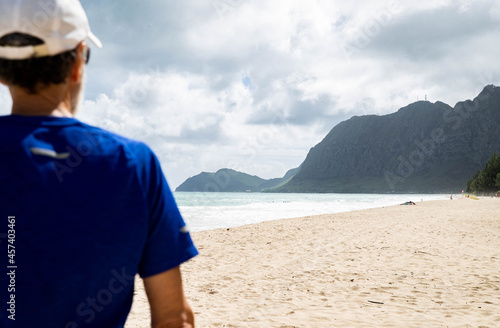 Serene man looking at mountain view while standing on a beach in Hawai