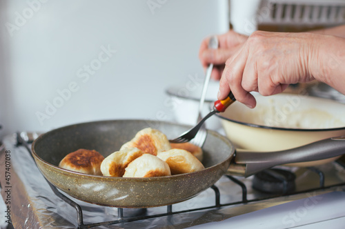 Hands flip donuts with forks in frying pan. Bowl of dough on stove