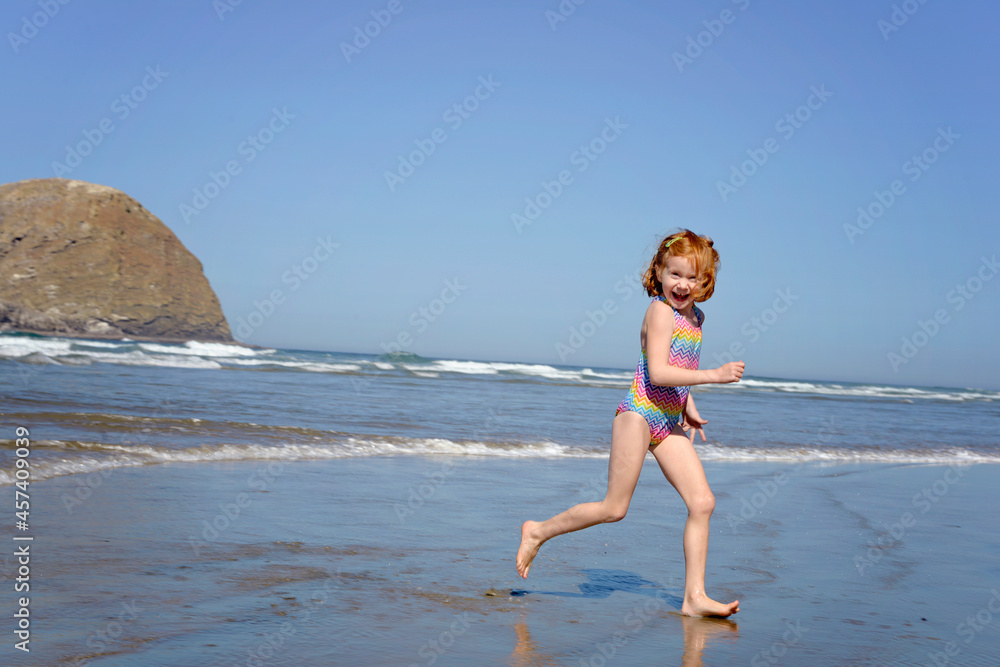 Happy little redhead girl running along the ocean shore.
