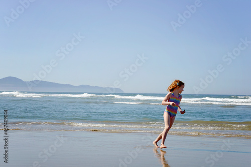 Happy little redhead girl running along the ocean shore.