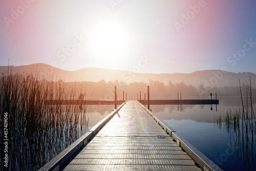 Beautiful sunrise over a lake and dock, mountains in background.