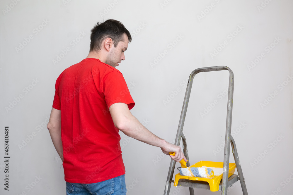 Man priming the wall with a roller. Repair of the interior. Young male decorator painting a wall in the empty room. Concept renovation do it yourself Man priming the wall with a roller. Repair of the interior. Young male decorator painting a wall in the empty room. Concept renovation do it yourself