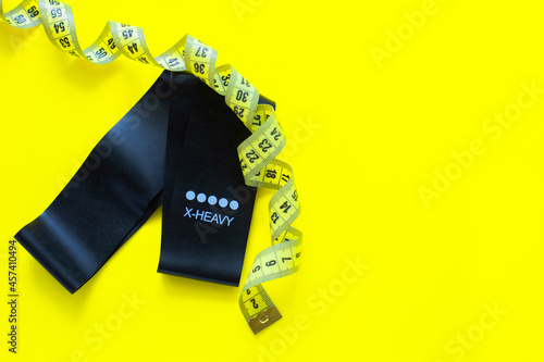 A black fitness elastic band lies on a yellow background, it is wrapped around a yellow measuring tape. top view, flat lay, copy space, isolate. photo