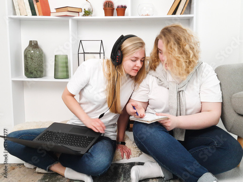 two women studying sitting on the floor with laptop and headphones photo