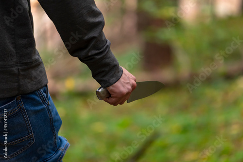  A man with a large knife in the forest, close-up, selective focus. Concept: attack on passers-by, rapist and murderer, crime in the forest belt, criminal and horror.