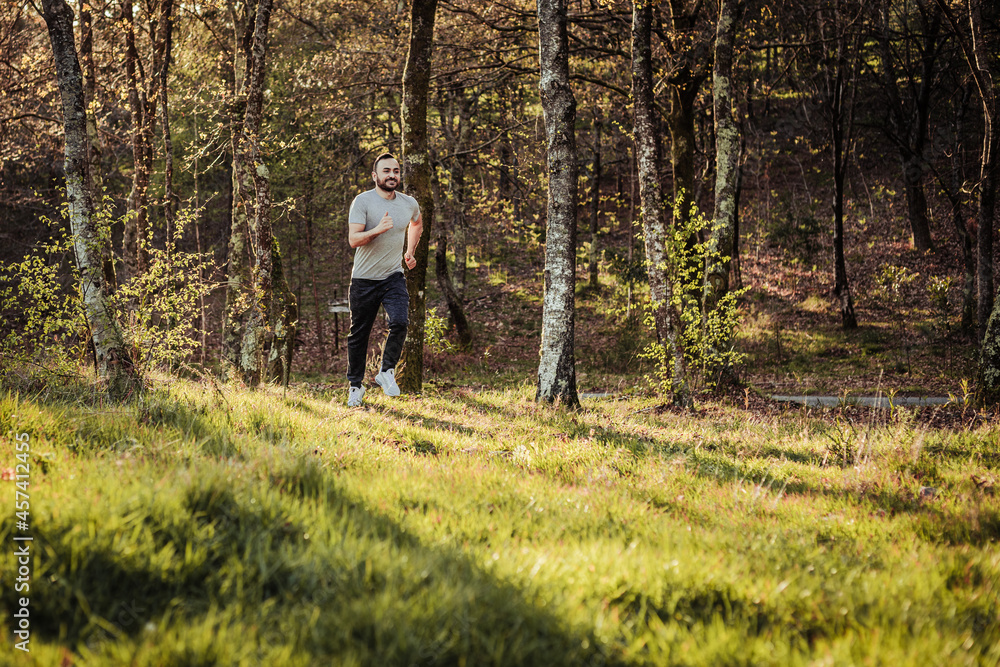 Man in cap and dark tracksuit running through the forest Man in cap and dark tracksuit running through the forest