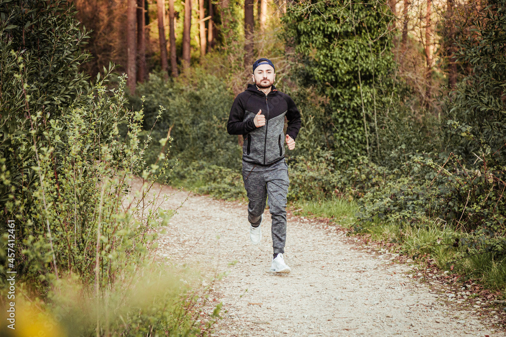 Man in cap and dark tracksuit running through the forest Man in cap and dark tracksuit running through the forest