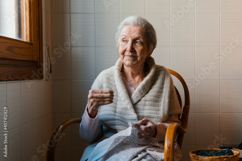 grandmother sews with needle and thread while looking out the window photo