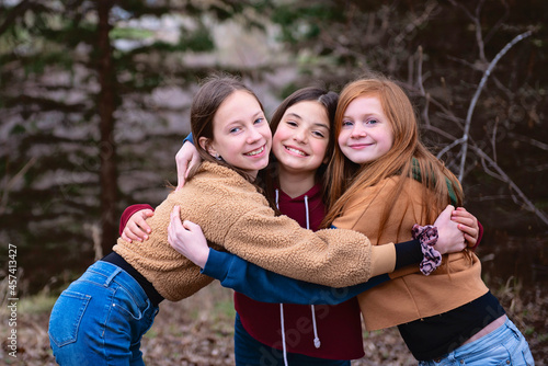 Three tween girls standing outdoors hugging each other. photo
