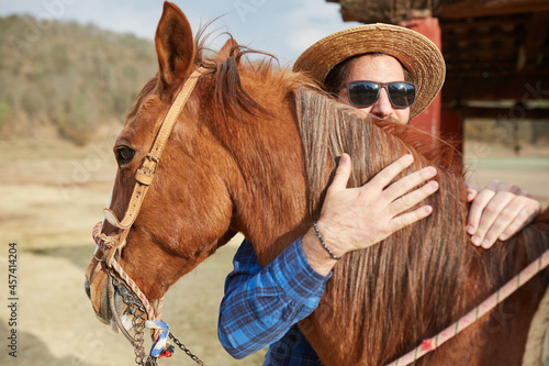 young man hat and beard hugging his horse in the field photo