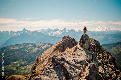 Hiker stands on summit of mountain with scenic view behind. photo