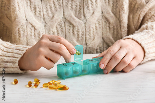 Woman putting fish oil pill in case at table, closeup