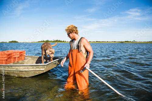 Young man working on the water in aquaculture oyster farm with dog photo